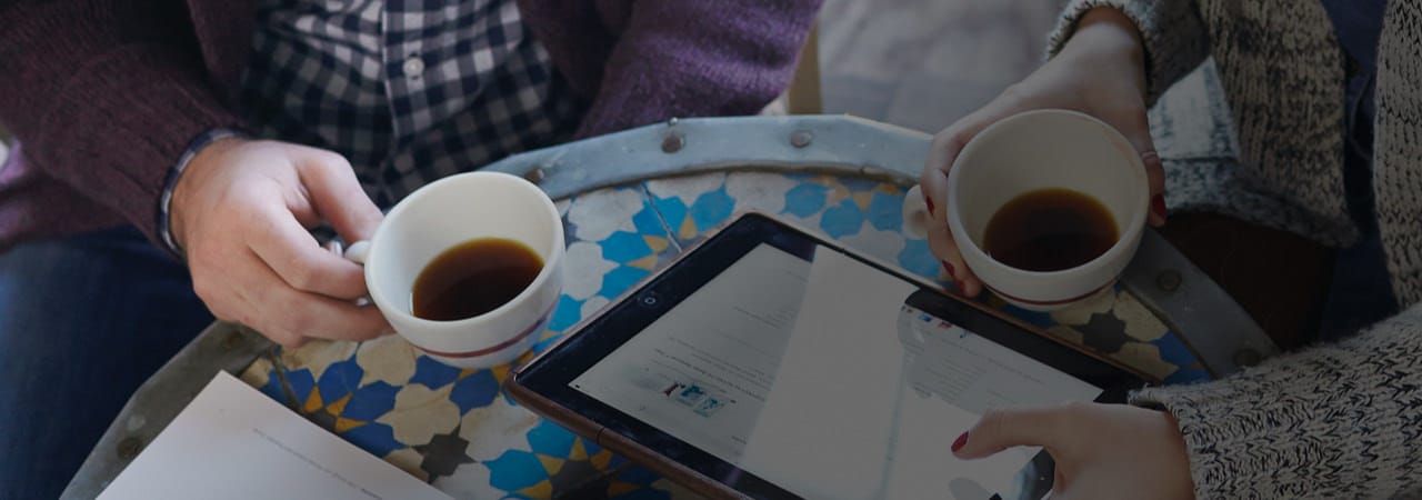 Una pareja tomando café, viendo el sitio web de Amway en una tableta. Conoce lo que otras personas dicen sobre nuestra oportunidad de negocio Amway.